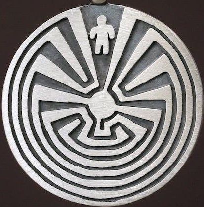 May include: A silver pendant necklace with a black cord. The pendant features a circular design with a labyrinth pattern and a small figure in the center.